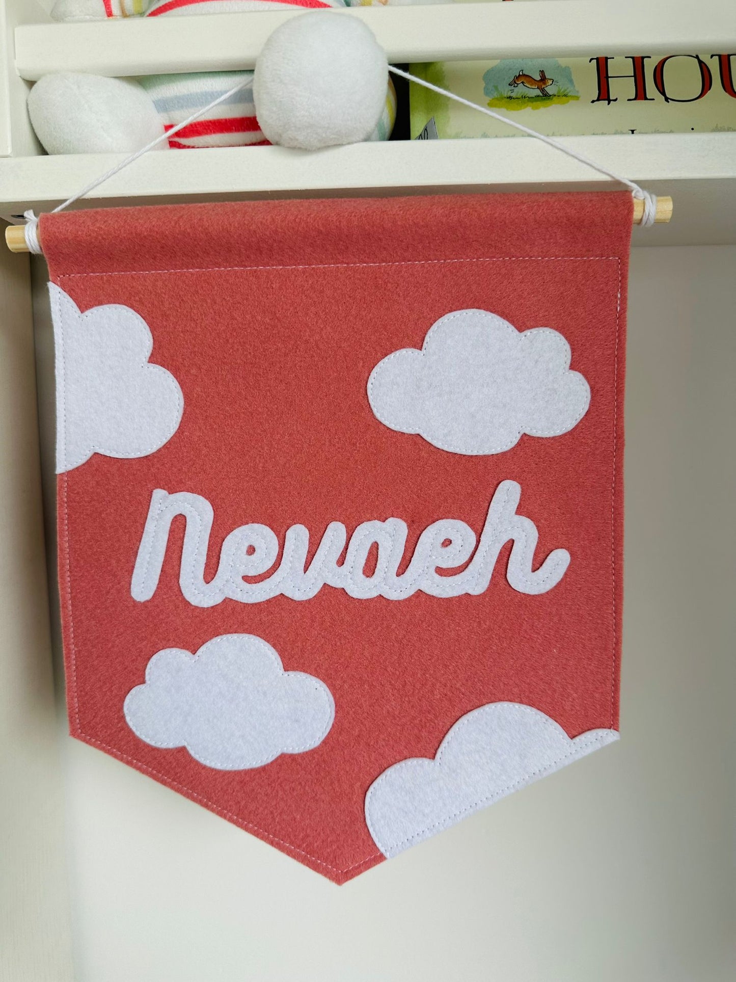 Gepersonaliseerde handgemaakte vilten banner met de naam "Nevaeh", bestaande uit oud roze kleurige banner met witte vilten letters wolken iconen. De randen van de banner is afgewerkt met een rechte rand. De banner hangt aan een wit katoenen koord aan een houten stok in een 