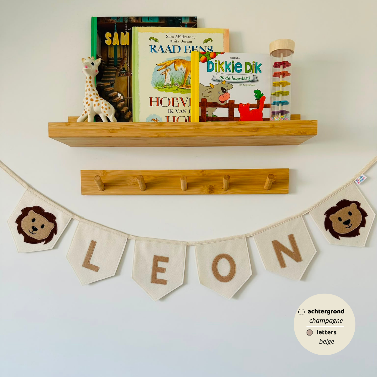 Gepersonaliseerde handgemaakte vilten naamvlaggenlijn met de naam "LEON", bestaande uit champagne kleurige vlaggen met beige vilten letters en bruin beige leeuwenhoofd op het eerste vlaggetje en het laatste vlaggetje. De randen van de vlaggen zijn afgewerkt met een rechte afwerking. De vlaggenlijn hangt aan een naturel katoenen lint.