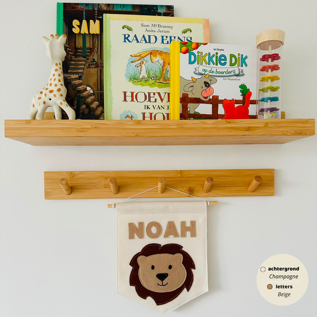 Gepersonaliseerde handgemaakte vilten banner met de naam "Noah", bestaande uit champagne kleurige banner met beige vilten letters en leeuwenhoofd icoon. De randen van de banner is afgewerkt met een rechte rand. De banner hangt aan een wit katoenen koord aan een houten stok in een kinderkamer.
