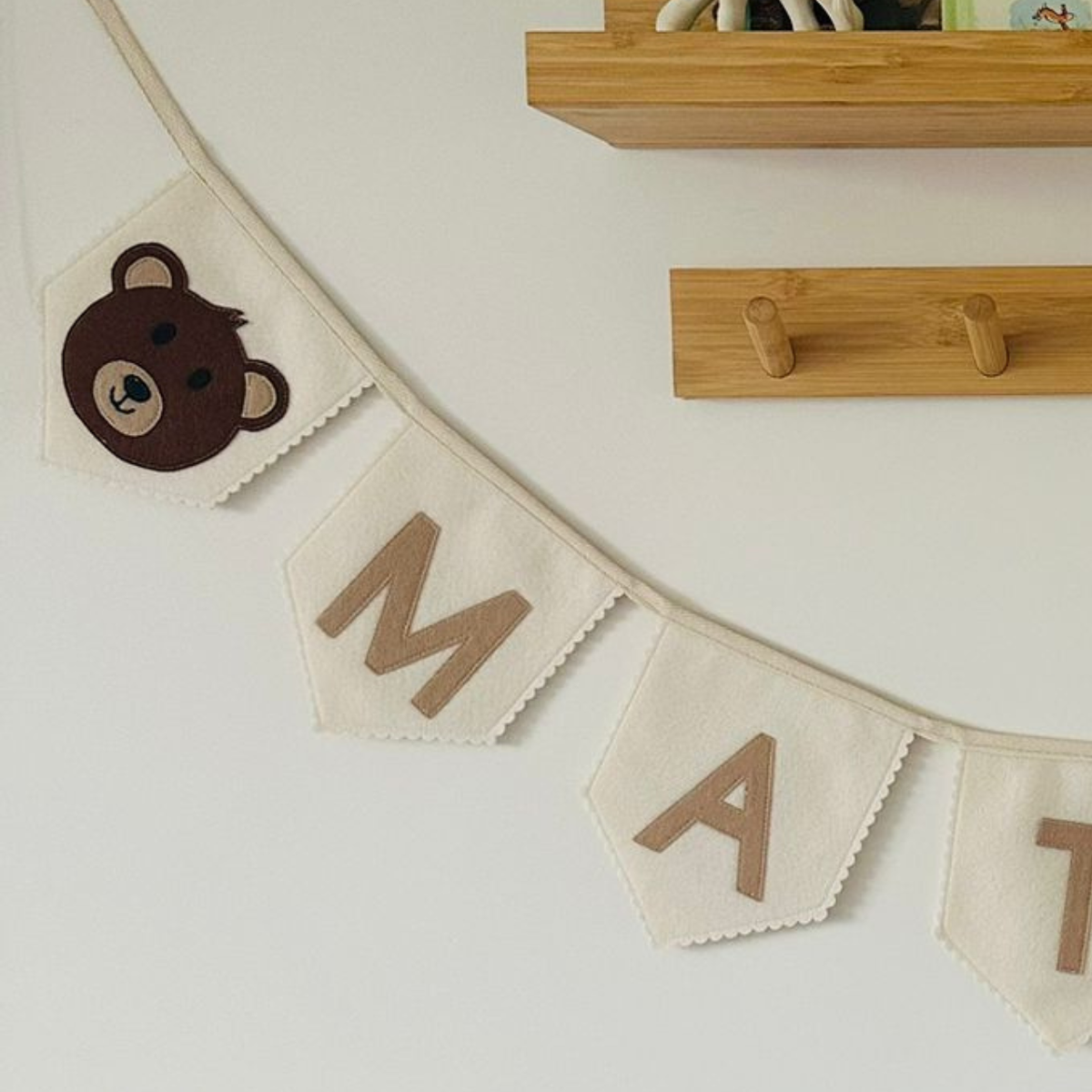 Close-up van een handgemaakte champagne kleurige vlaggen met een bruin beertjes-icoon en de letters "M", "A" en "T" in beige vilt.