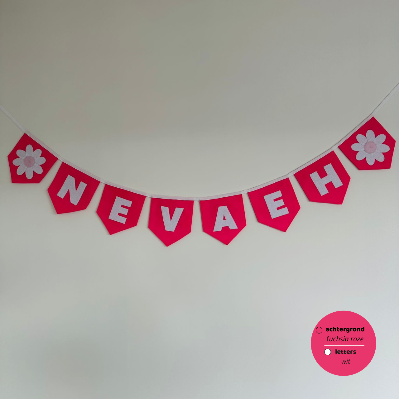 Gepersonaliseerde handgemaakte vilten naamvlaggenlijn met de naam "NEAVAEH", bestaande uit fuchsia roze kleurige vlaggen met witte vilten letters en wit met licht roze bloem op het eerste vlaggetje en het laatste vlaggetje. De randen van de vlaggen zijn afgewerkt met een rechte afwerking. De vlaggenlijn hangt aan een wit katoenen lint.