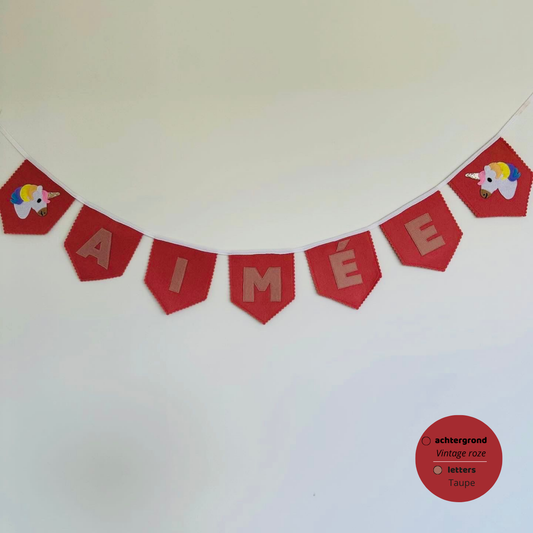 Gepersonaliseerde handgemaakte vilten naamvlaggenlijn met de naam "Aimee", bestaande uit Taupe kleurige vilten letters met Vintage roze vlaggen met een eenhoorn op het eerste vlaggetje en het laatste vlaggetje. De randen van de vlaggen zijn afgewerkt met een scalp afwerking. De vlaggenlijn hangt aan een wit katoenen lint.