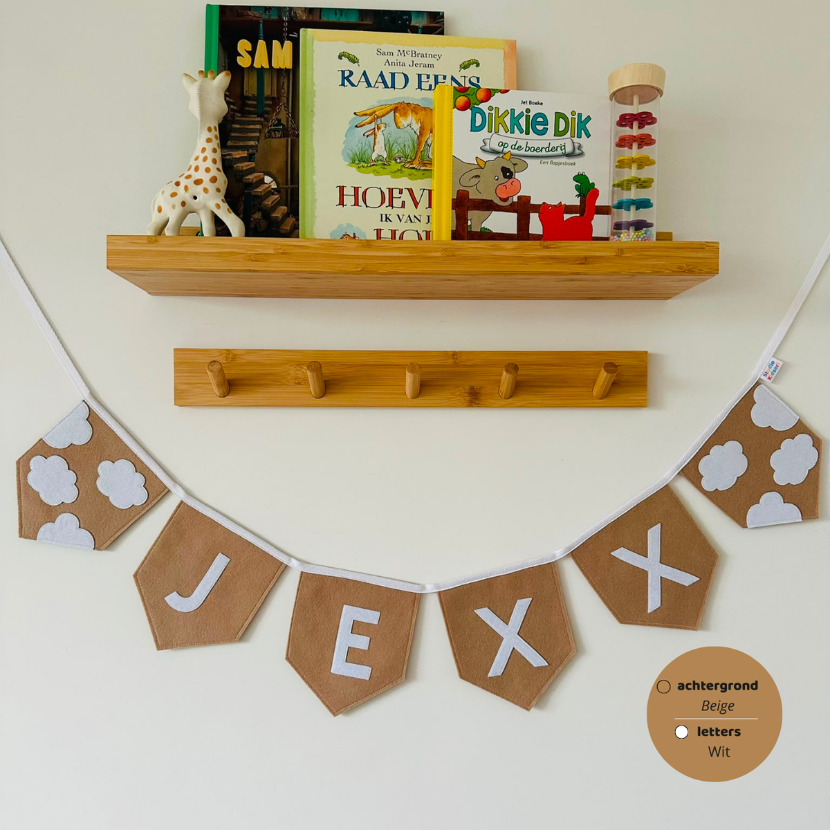Gepersonaliseerde handgemaakte vilten naamvlaggenlijn met de naam "Jexx", bestaande uit Taupe kleurige vilten vlaggen met witte letters met witte wolken op het eerste vlaggetje en het laatste vlaggetje. De randen van de vlaggen zijn afgewerkt met een rechte afwerking. De vlaggenlijn hangt aan een wit katoenen lint.