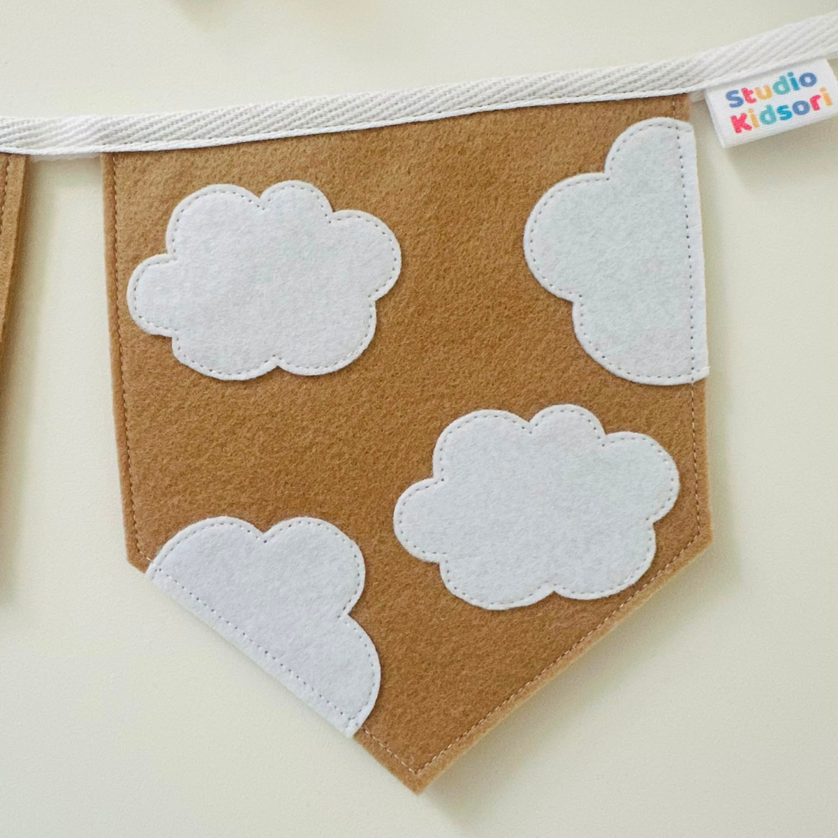 Handgemaakte vilten vlag met een wolken iconen erop, hangend aan een witte katoenen lint. De randen van de vlag zijn met een rechte afwerking afgewerkt.